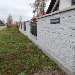 Nowoczesne ogrodzenie z szarego, łupanego kamienia z czarnymi, poziomymi przęsłami, tabliczka z adresem 'ul. Księżycowa 12'.