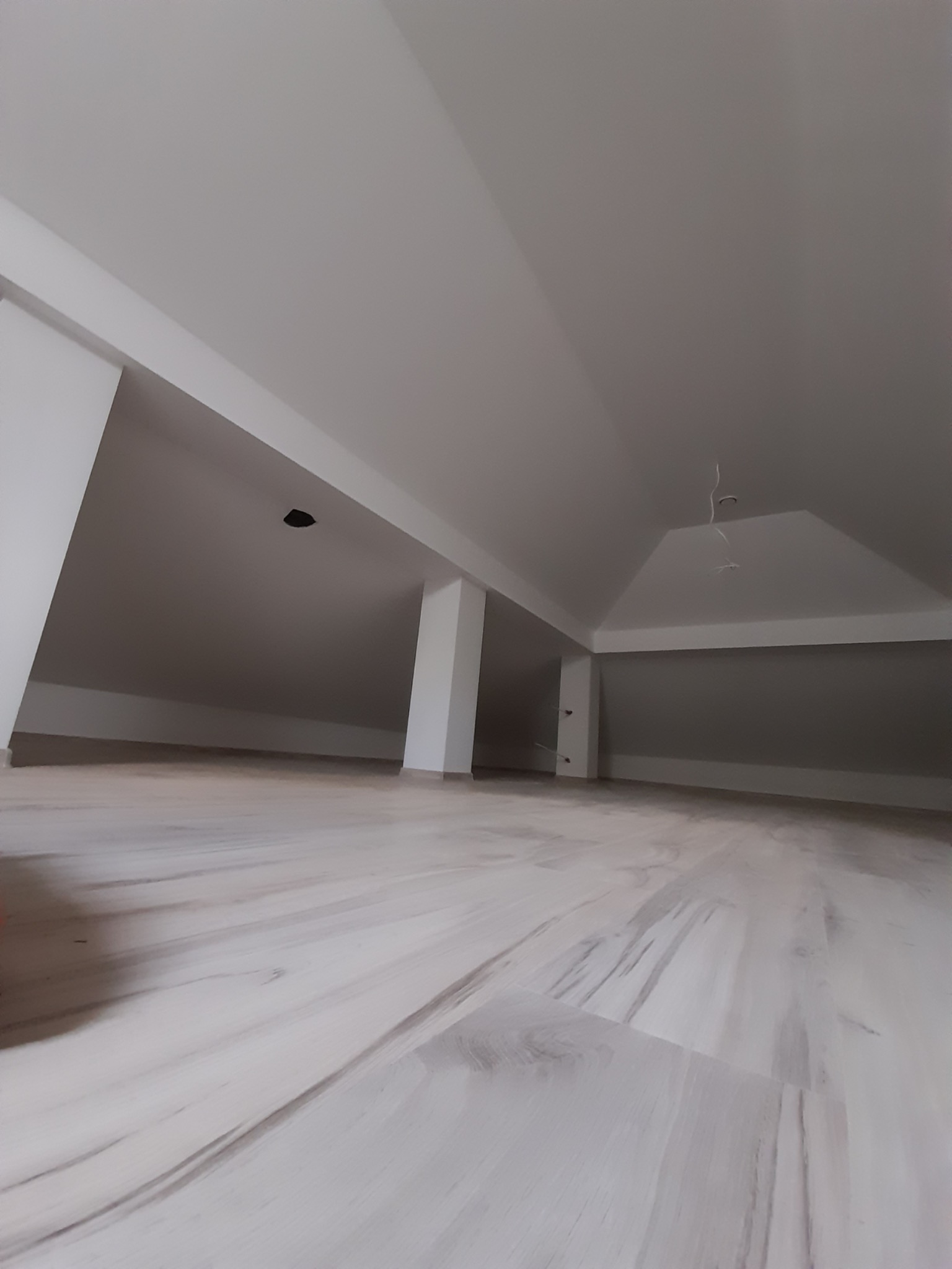 Poddasze po remoncie w Krakowie z nową podłogą imitującą drewno i świeżo pomalowanymi ścianami na biało, widoczne elementy instalacji elektrycznej.