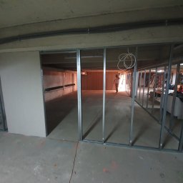 Usługi remontowe - Metalowy szkielet ścian działowych z płyt kartonowo-gipsowych w surowym wnętrzu, widoczna osoba w tle.