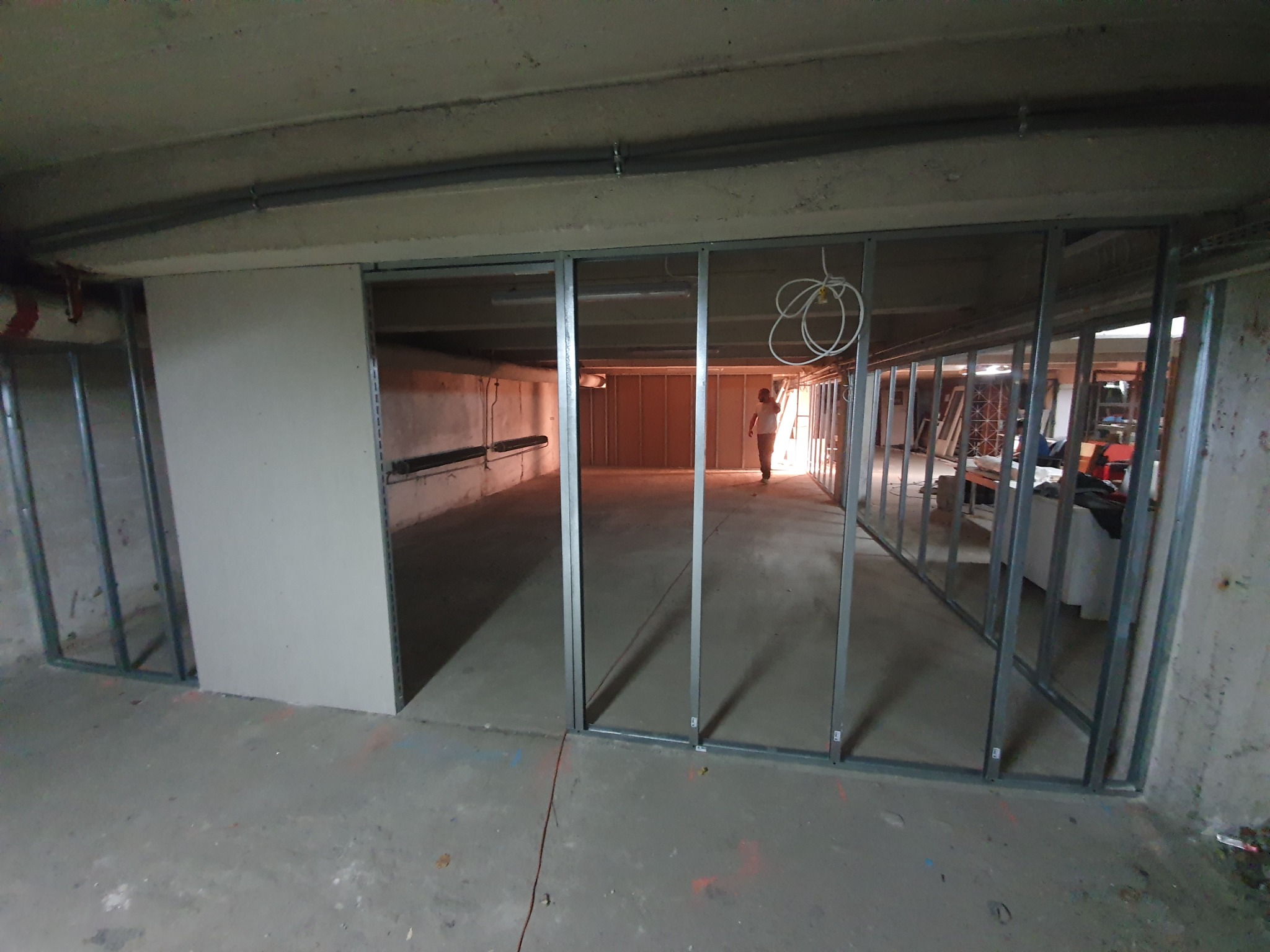 Metalowy szkielet ścian działowych z płyt kartonowo-gipsowych w surowym wnętrzu, widoczna osoba w tle.