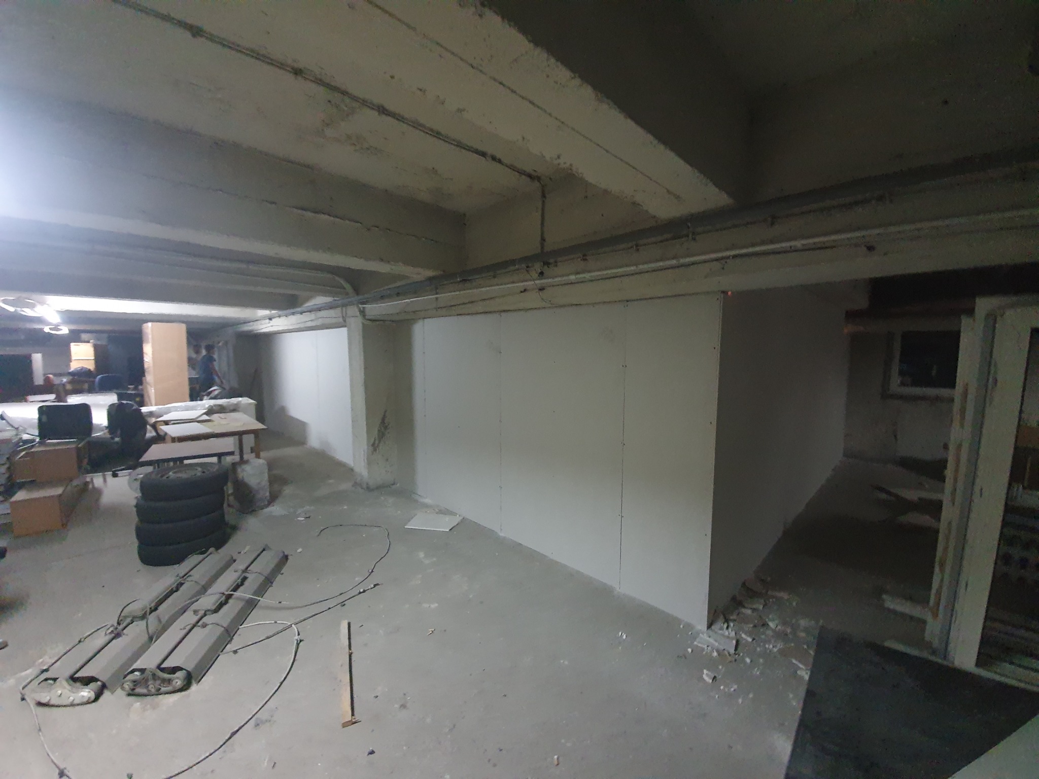 Montaż ścian działowych z płyt karton gips w piwnicy, widoczne narzędzia i opony, surowy betonowy strop