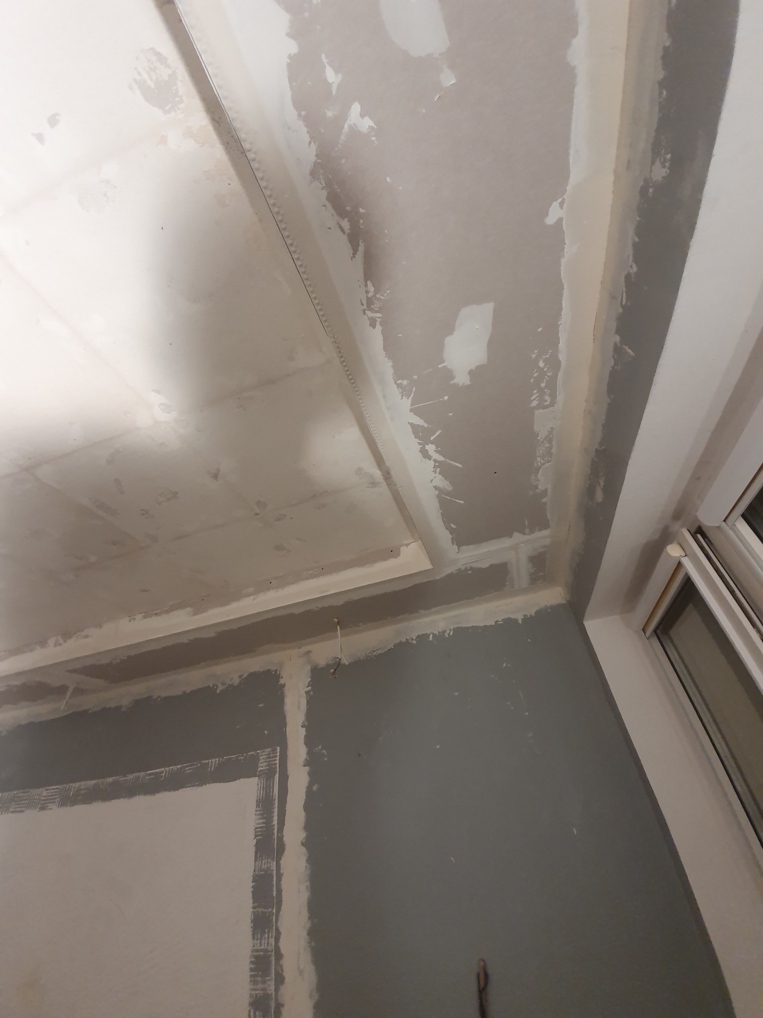 Prace przygotowawcze do malowania ścian i sufitu z płyty karton gips w Bydgoszczy, widoczne szpachlowanie łączeń i narożników, surowe wykończenie przy oknie.