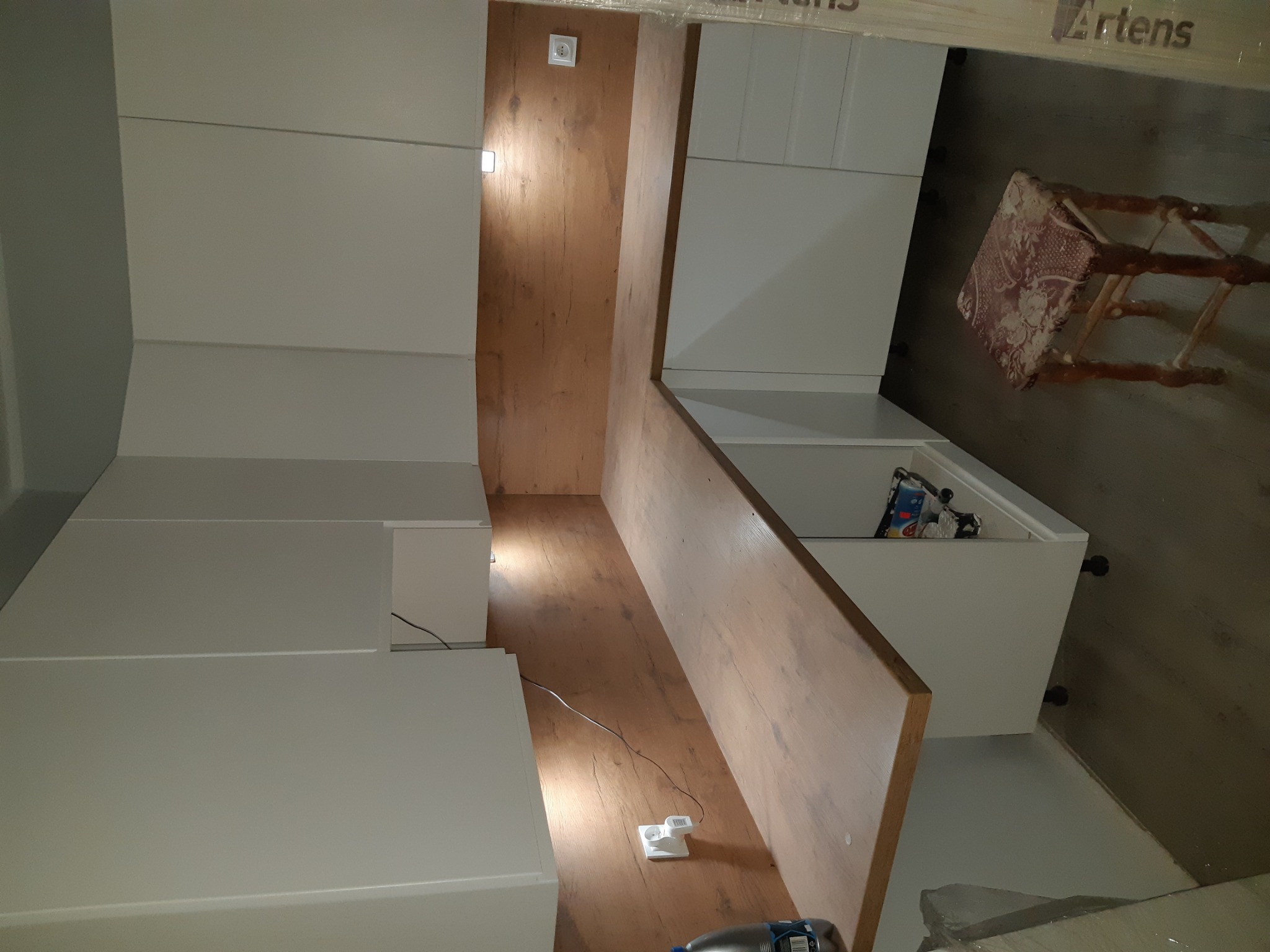 Nowoczesna zabudowa kuchenna z białymi frontami i drewnopodobnym blatem w Złotoryi, widok na wnętrze szafki z gniazdkiem elektrycznym i drobnymi przedmiotami.