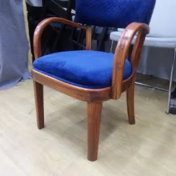 Odnowione krzesło z drewnianą ramą i nową, niebieską tapicerką z pikowaniem na oparciu i siedzisku, stojące na podłodze w warsztacie.