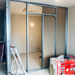 Kompleksowe wykończenia i koorydnacja prac remontowych - Montaż ścianki działowej z profili stalowych i płyt gipsowo-kartonowych, widoczna drabina i opakowanie wełny mineralnej Rockwool, surowy stan wykończenia.