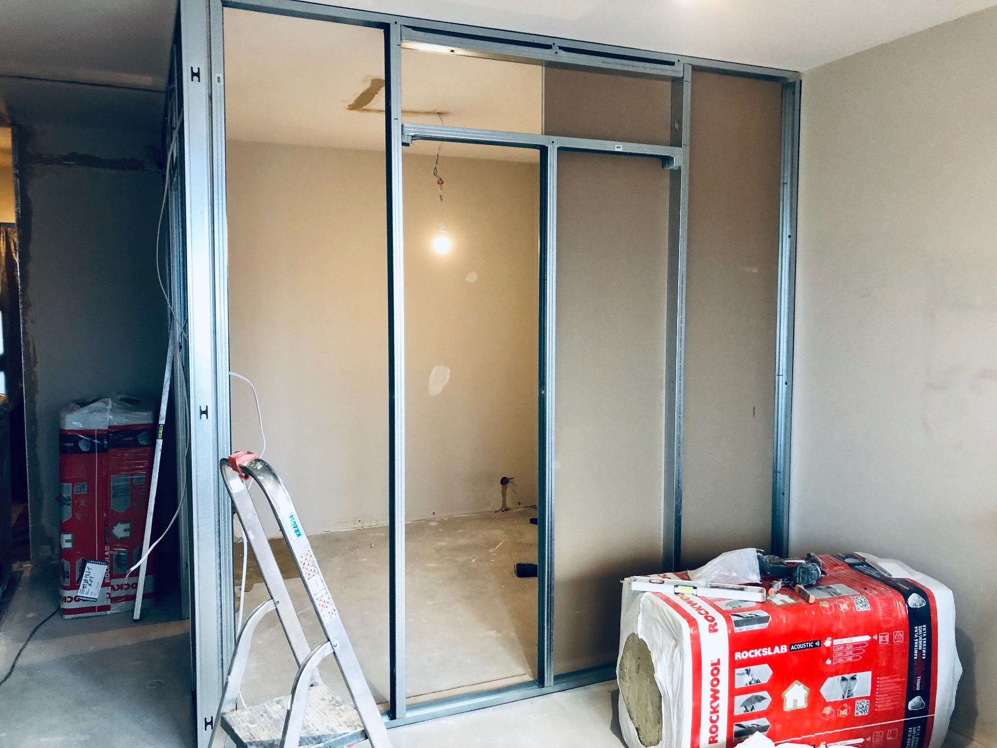 Montaż ścianki działowej z profili stalowych i płyt gipsowo-kartonowych, widoczna drabina i opakowanie wełny mineralnej Rockwool, surowy stan wykończenia.