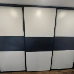 Trzydrzwiowa szafa przesuwna z czarnymi ramami i poziomym pasem w kolorze czarnym, z białymi panelami powyżej i poniżej, widok z dołu.