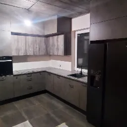 Nowoczesna kuchnia w odcieniach szarości z drewnopodobnymi szafkami górnymi, czarnym piekarnikiem i lodówką Haier, widok na łazienkę w tle.