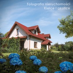 Gocha Chmiel Fotografia i Film - Jasny dom jednorodzinny z czerwonym dachem, otoczony zielenią i niebieskimi hortensjami w słoneczny dzień. Ujęcie z poziomu ogrodu, widok na fasadę i dach.