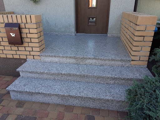 Zewnętrzne schody wejściowe z szarego, nakrapianego kamienia prowadzące do drzwi, z ceglanymi filarami po bokach i brązową skrzynką na listy.