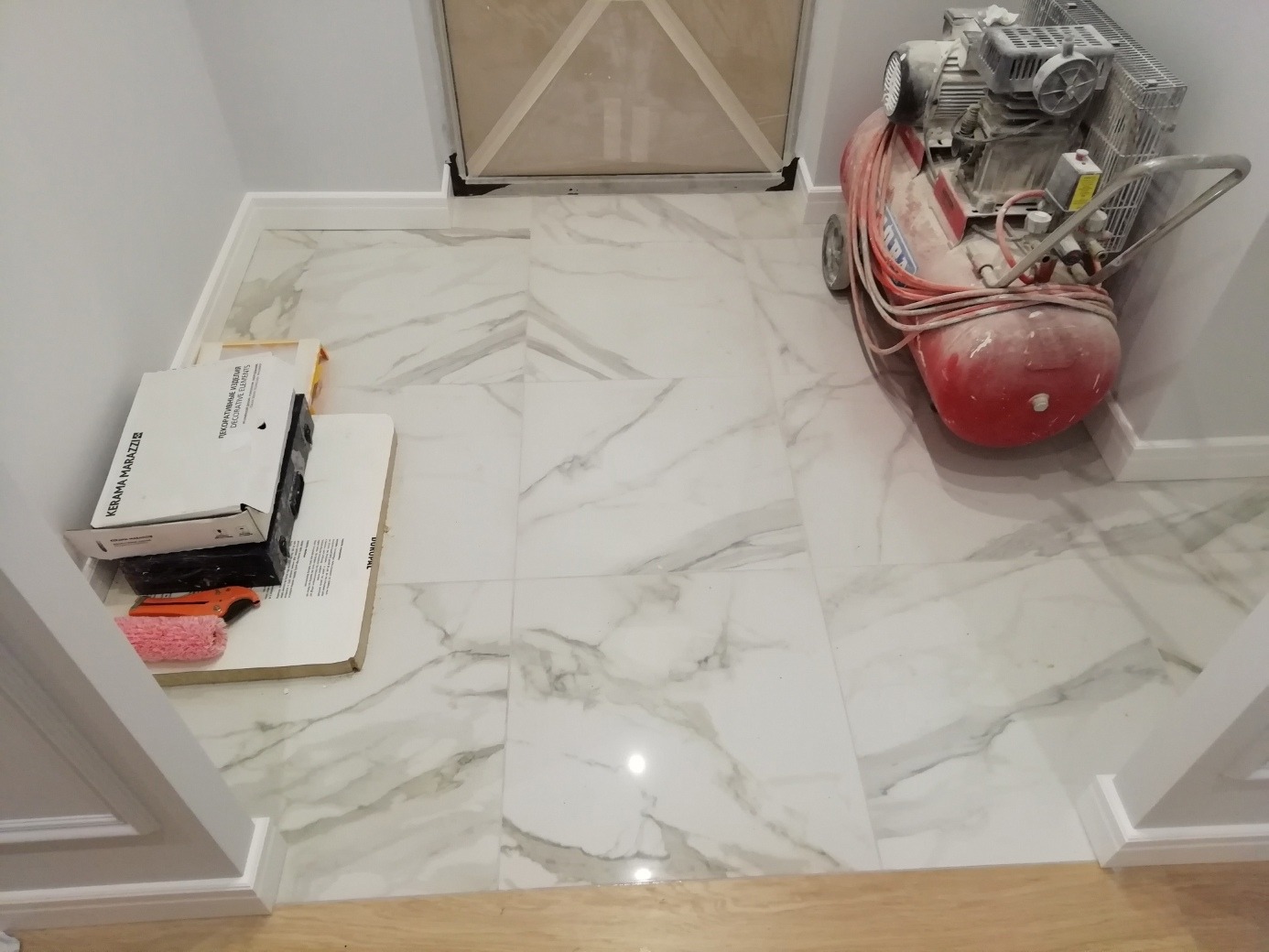 Wyłożona marmurowymi płytkami podłoga w przedpokoju, widoczny kompresor i kartony z płytkami oraz narzędzia glazurnicze.