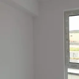 Pomieszczenie po malowaniu na biało, widok na narożnik i okno PCV z widokiem na zewnątrz.