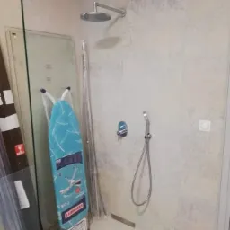 Nowoczesna kabina prysznicowa z deszczownicą i słuchawką, widoczna deska do prasowania Leifheit oparta o ścianę, płytki imitujące kamień