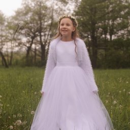 Jakub Kowalski - Uśmiechnięta dziewczynka w białej sukience komunijnej i wianku na łące w Sosnowcu. Delikatne światło, naturalne tło drzew. Sesja komunijna w plenerze.
