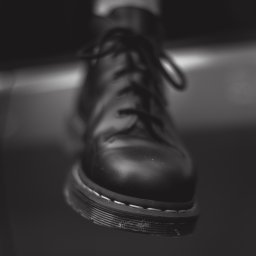 Jakub Kowalski - Czarno-białe zbliżenie na czarny, skórzany but z sznurowadłami, ustawiony pod kątem. Widoczna charakterystyczna podeszwa z białym przeszyciem i detale skóry.