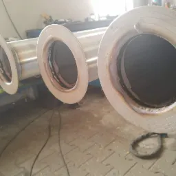 Spojenia spawane trzech rur ze stali nierdzewnej z kołnierzami, widoczne ślady spawania, w tle warsztat.