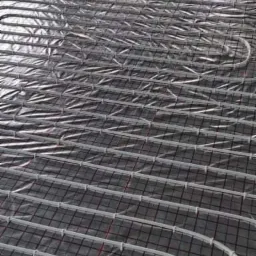 Instalacja ogrzewania podłogowego w nowym budynku, widoczne rury grzewcze na folii izolacyjnej z siatką, przygotowane do zalania wylewką.