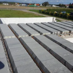 Wiązanie zbrojeniowe stropu Teriva z widocznymi belkami i pustakami stropowymi na budowie domu jednorodzinnego, z zielonym terenem w tle.