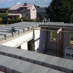 Wznoszenie ścian domu z betonu komórkowego, widoczne zbrojenie stropu i pustaki H+H na budowie w słoneczny dzień.