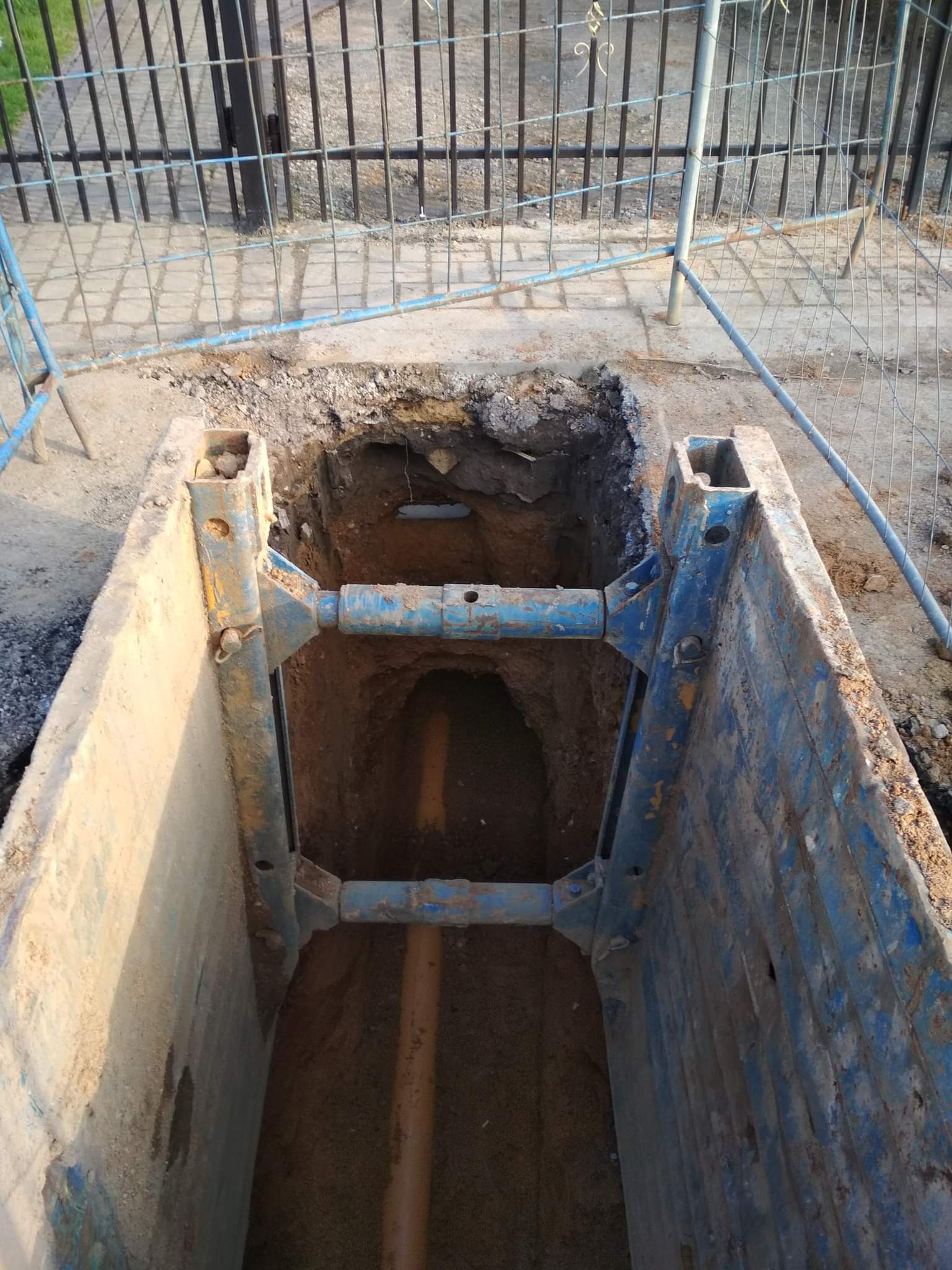Wykonany wykop z zabezpieczeniami ścian, widoczny rurociąg w ziemi oraz siatka ogrodzeniowa w tle.