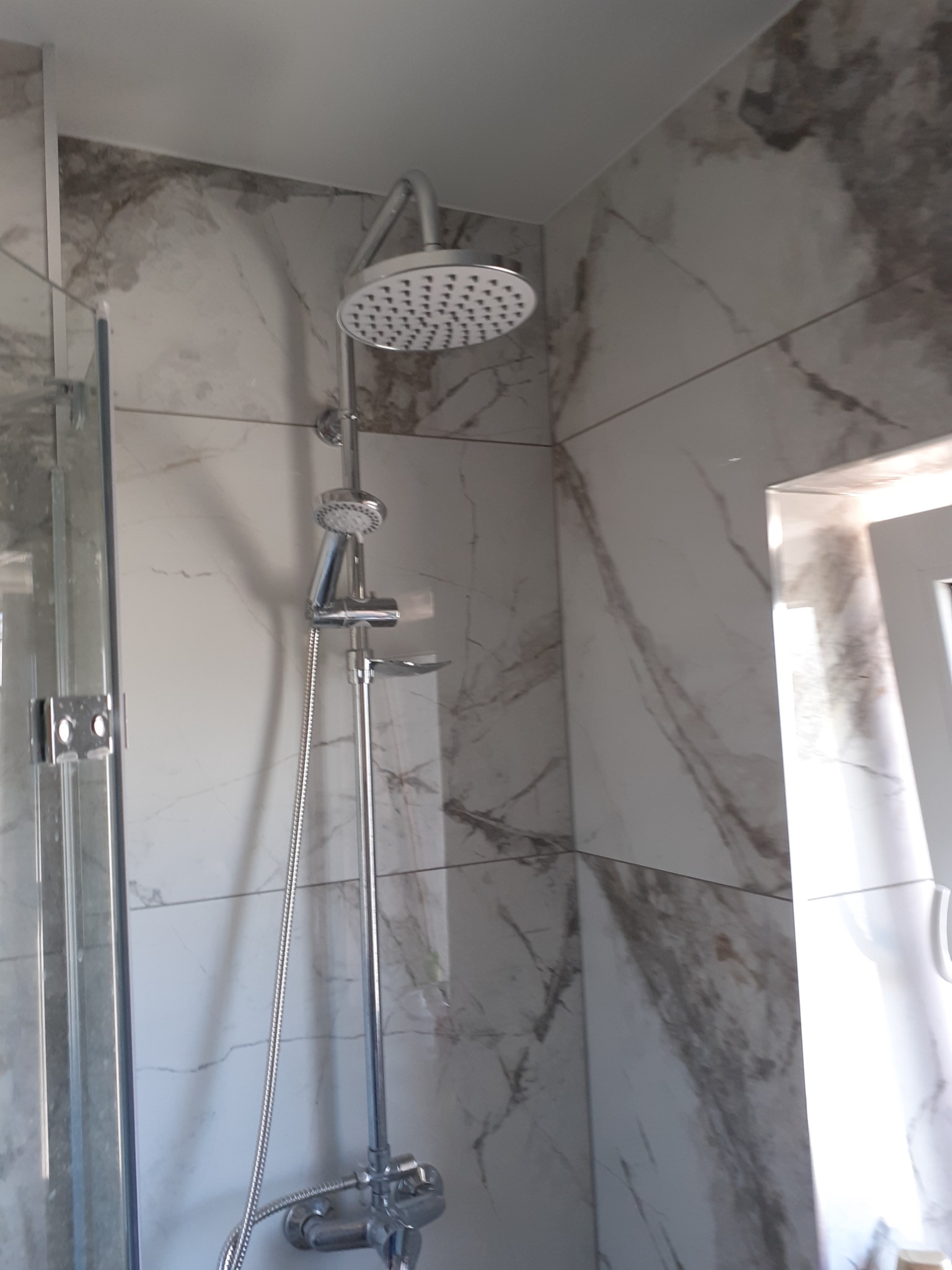 Nowoczesna kabina prysznicowa z deszczownicą i baterią termostatyczną, wykończona płytkami imitującymi marmur.