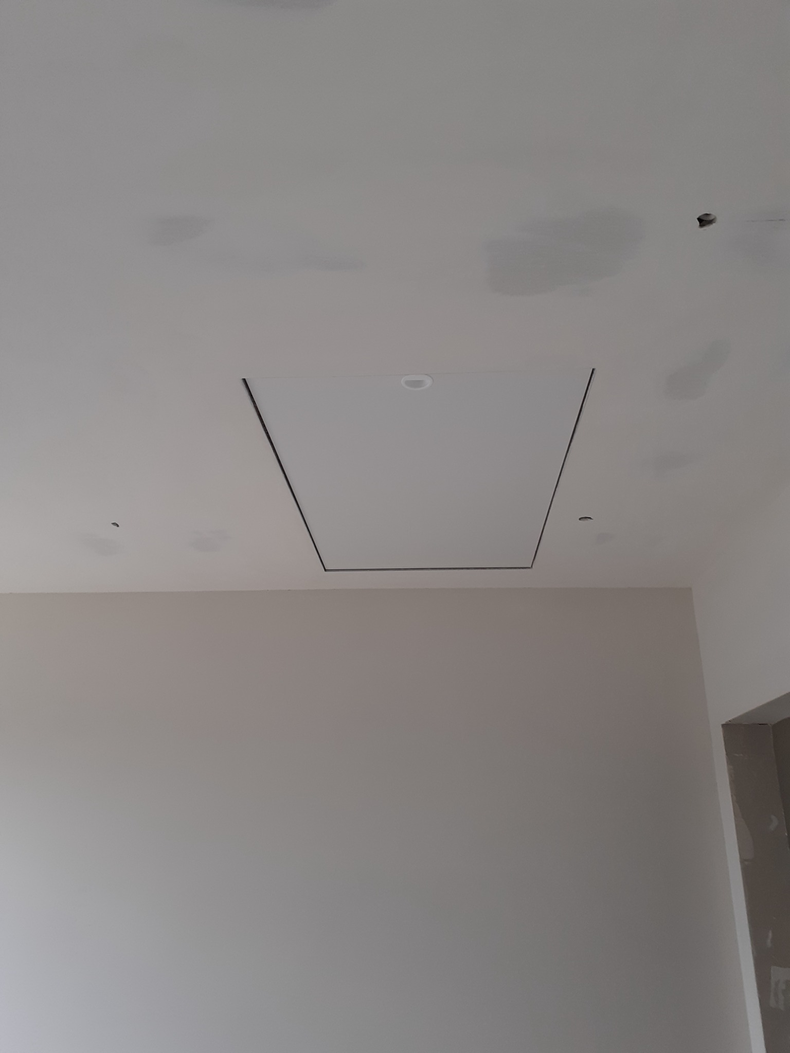 Biały sufit z zamontowaną klapą rewizyjną z czarną obwódką i wbudowanym oświetleniem punktowym, widoczne ślady po szpachlowaniu i otwór na instalację.