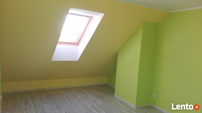 Pomalowane na żółto poddasze z oknem dachowym i świeżo położonymi panelami podłogowymi w odcieniach szarości.