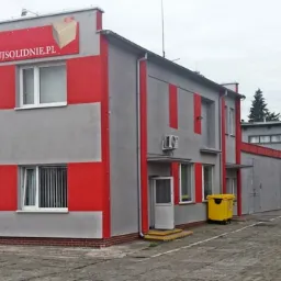 Budynek firmy ITax z logo i hasłem 'pakujsolidnie.pl', szaro-czerwona fasada, żółty kontener na śmieci przed wejściem.