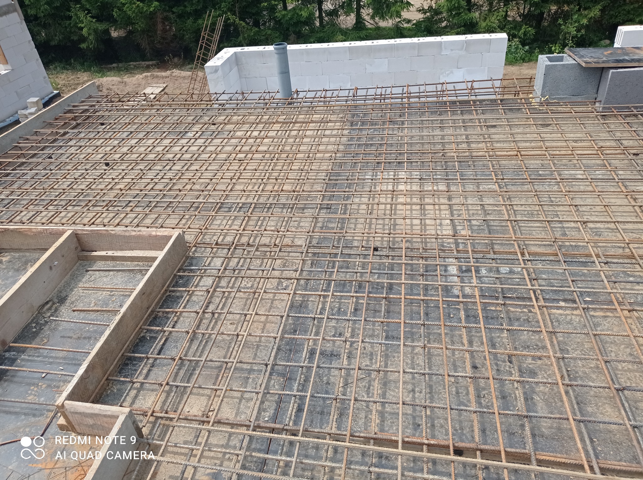 Zbrojenie płyty stropowej z siatki stalowej na budowie domu jednorodzinnego, widoczne bloczki betonowe i drewniane szalunki.