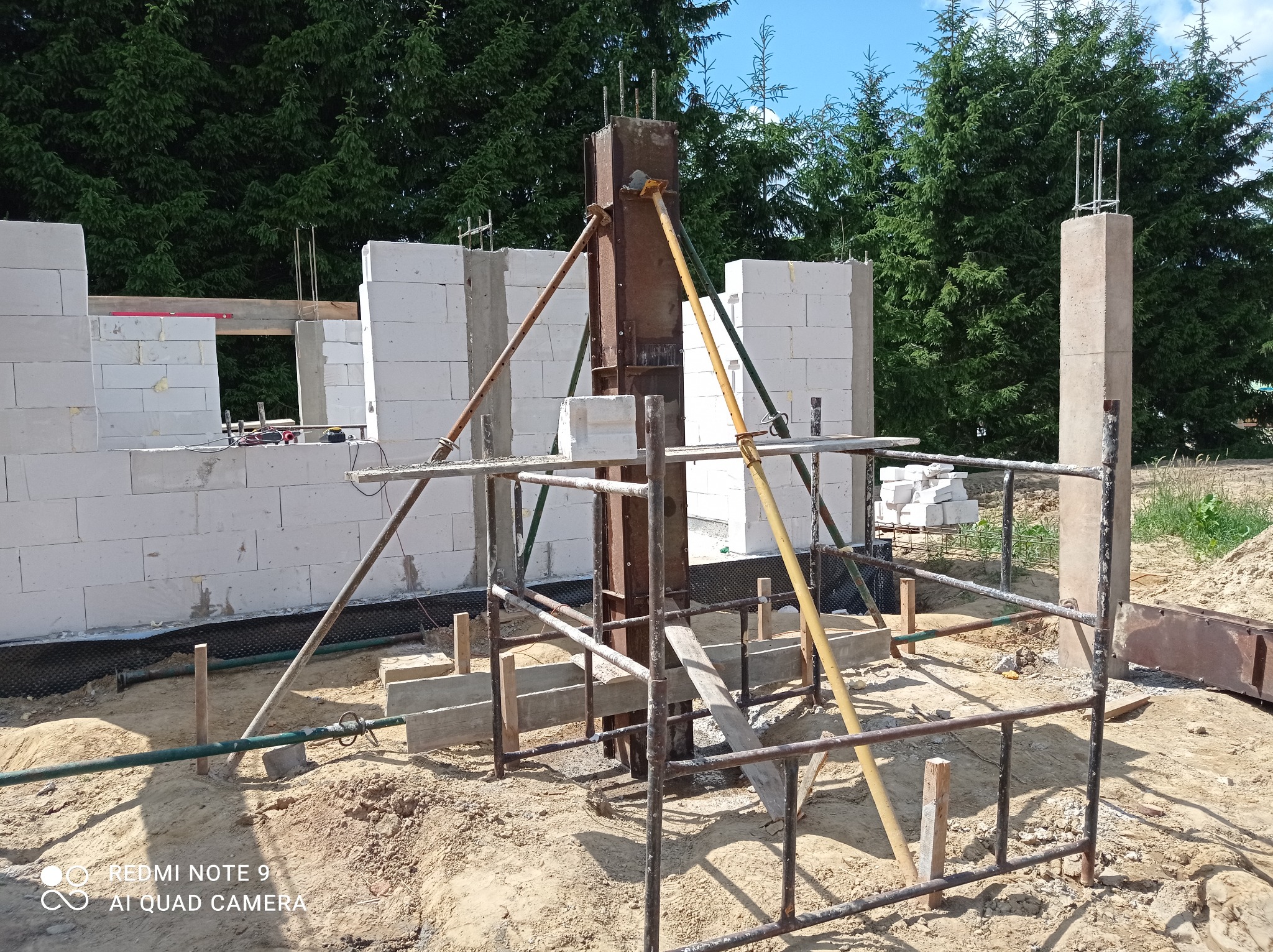Budowa domu z betonu komórkowego: wznoszenie ścian i szalowanie słupów, widoczne zbrojenia i podpory szalunków.