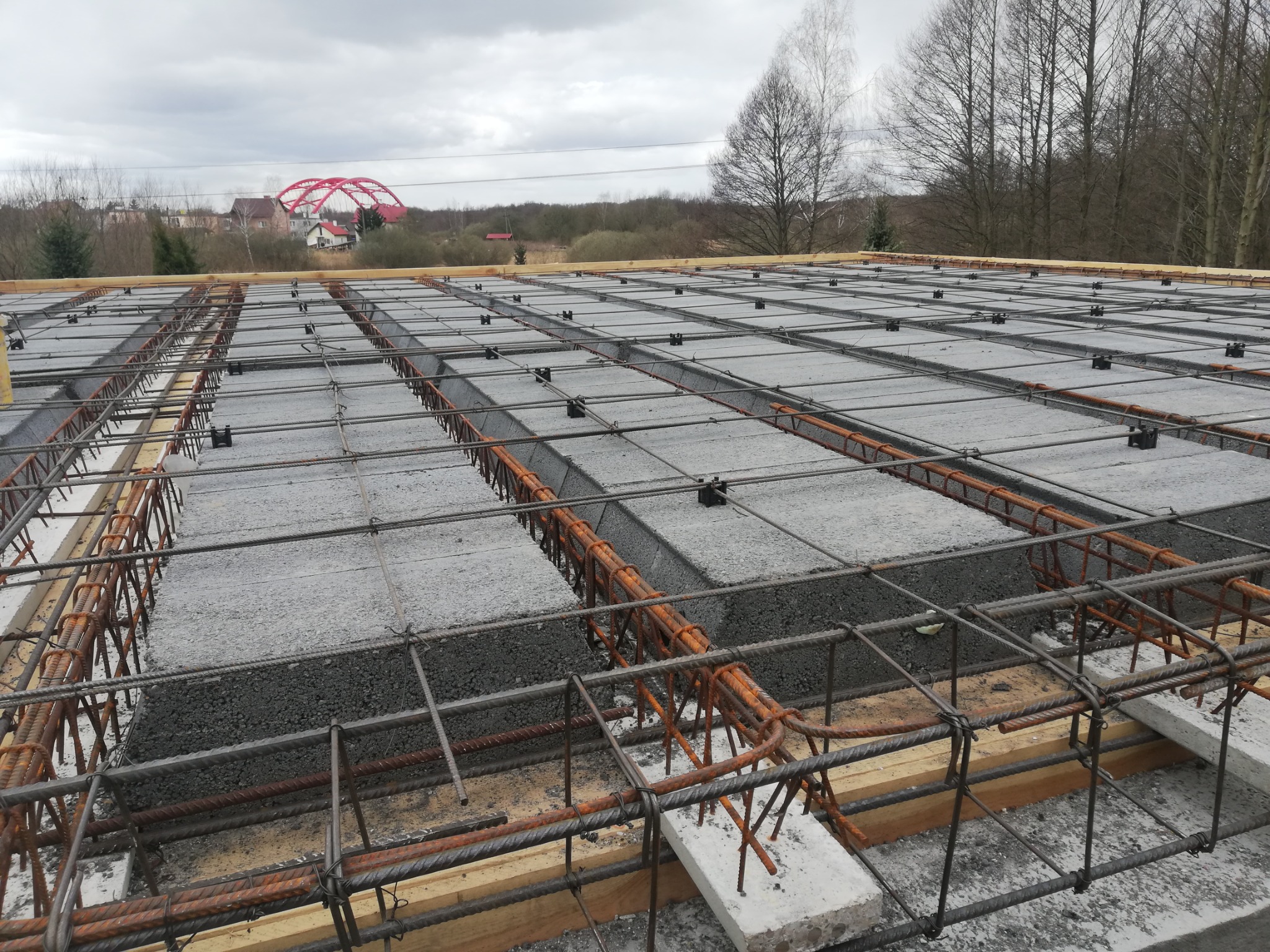 Siatka zbrojeniowa na stropie Teriva przed zalaniem betonem, widoczny czerwony most w tle.