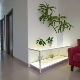 Podświetlana ściana z onyksu obok dwóch drzwi, biały regał z podświetlanymi półkami z onyksu i roślinami doniczkowymi, fragment czerwonej sofy.