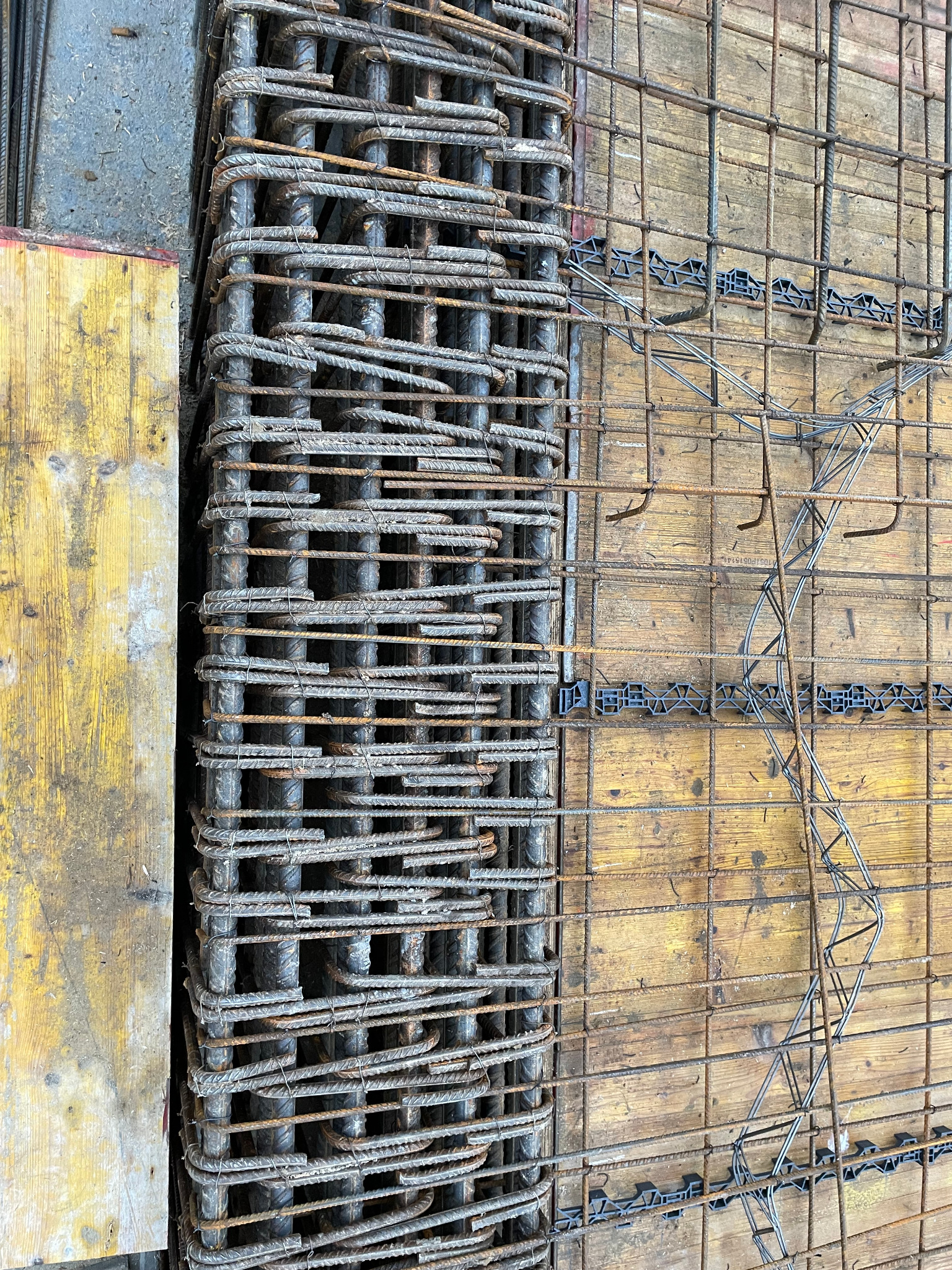 Przygotowane zbrojenie na budowie w Warszawie, ułożone obok drewnianego szalunku. Widoczne elementy dystansowe z tworzywa sztucznego.
