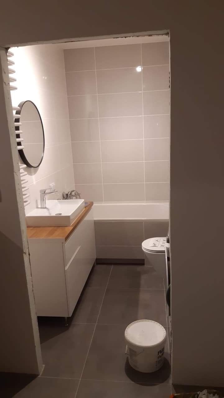 Wykończona łazienka w Warszawie z beżowymi płytkami na ścianach, brązowymi płytkami na podłodze, białymi szafkami pod umywalką z drewnianym blatem i okrągłym lustrem.