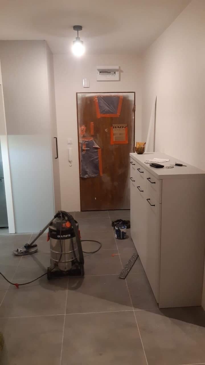 Korytarz w trakcie remontu: zabezpieczone drzwi wejściowe, odkurzacz przemysłowy, pomalowane ściany i szare płytki podłogowe.