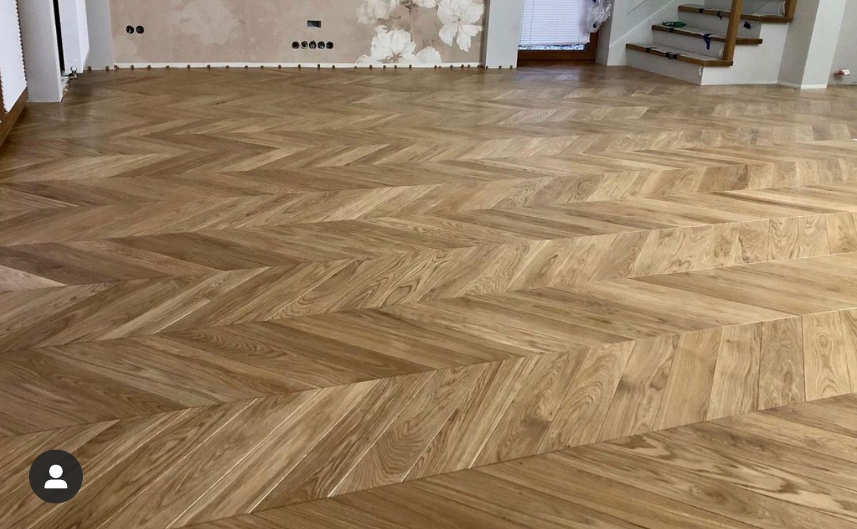 Ułożony parkiet w jodełkę francuską z drewna dębowego, widoczne przejście między poziomami podłogi, ściana z dekoracyjną tapetą w kwiaty w tle.