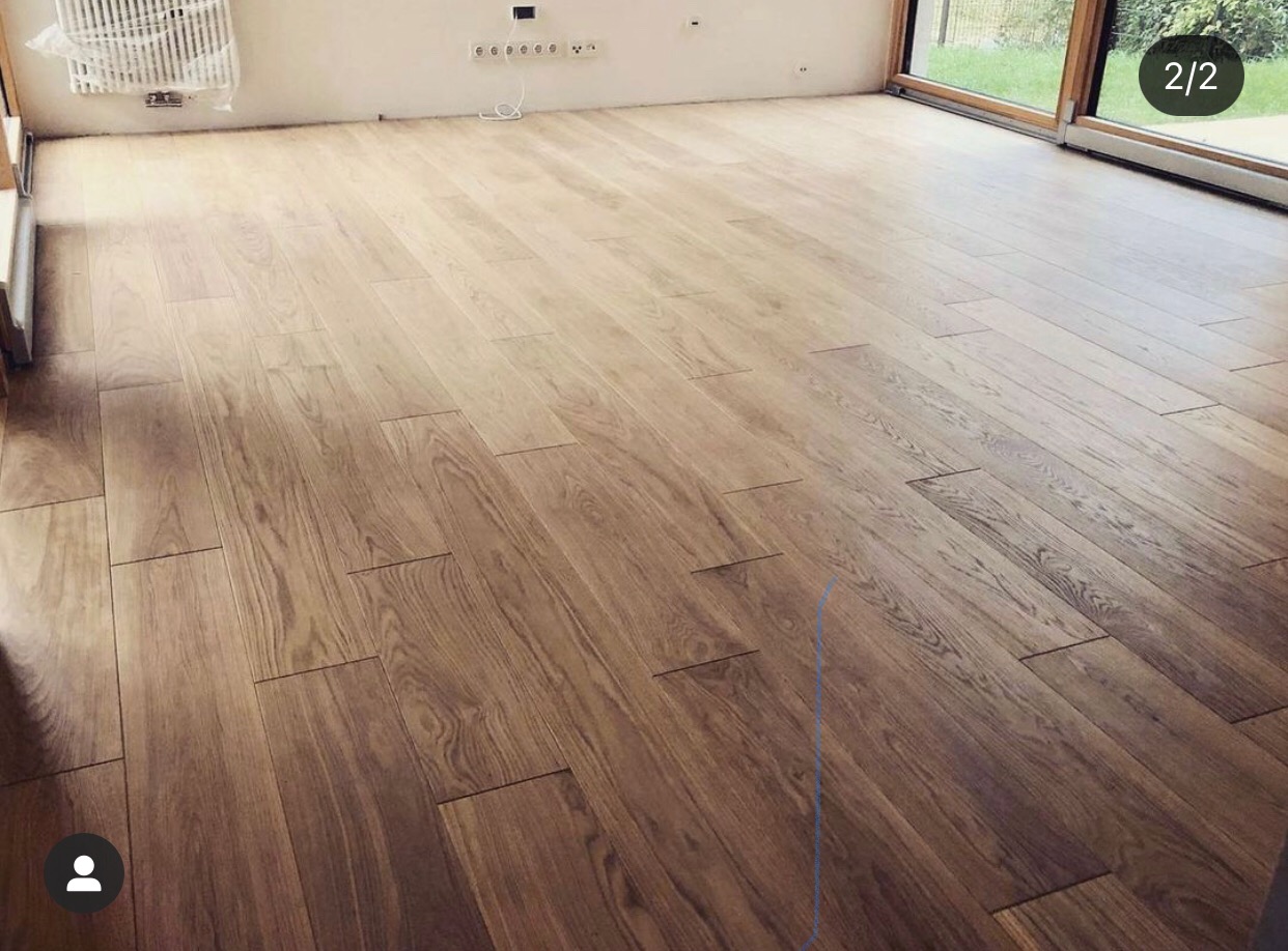 Ukończona podłoga z parkietu drewnianego ułożonego w jodełkę, widok na jasne, przestronne wnętrze z oknem i grzejnikiem na ścianie.