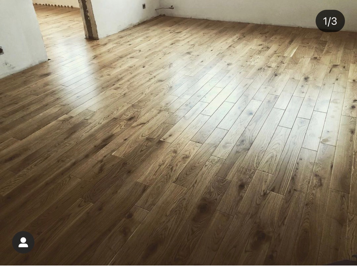 Ułożony parkiet z naturalnego drewna w jasnym odcieniu, widoczny fragment ściany w trakcie wykańczania.