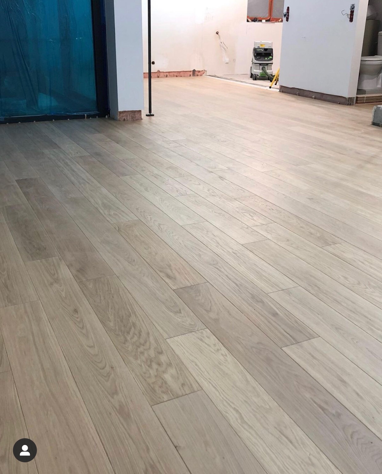 Jasne panele podłogowe ułożone w jodełkę, widoczny odkurzacz przemysłowy i przygotowania do dalszych prac wykończeniowych w tle.