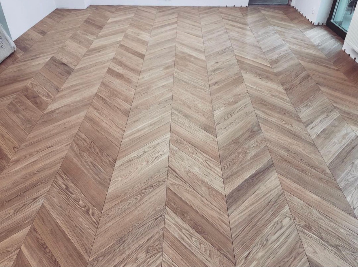 Jasnobrązowy parkiet ułożony we wzór jodełki francuskiej, widok z góry na całą powierzchnię podłogi w jasnym pomieszczeniu.