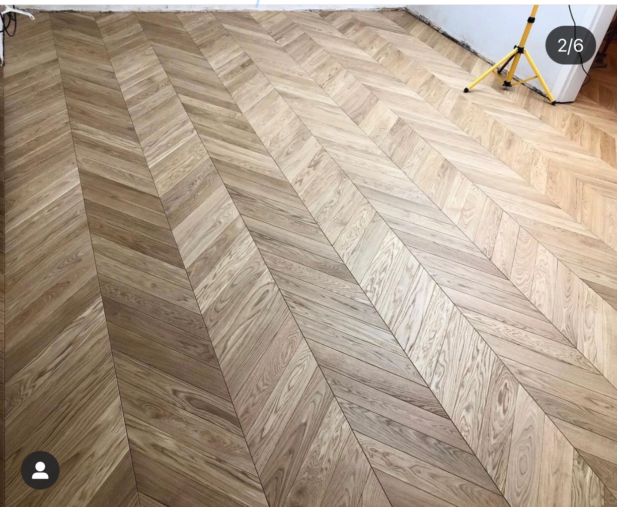 Ułożony parkiet w jodełkę z naturalnego drewna, oświetlony lampą budowlaną w rogu pomieszczenia.