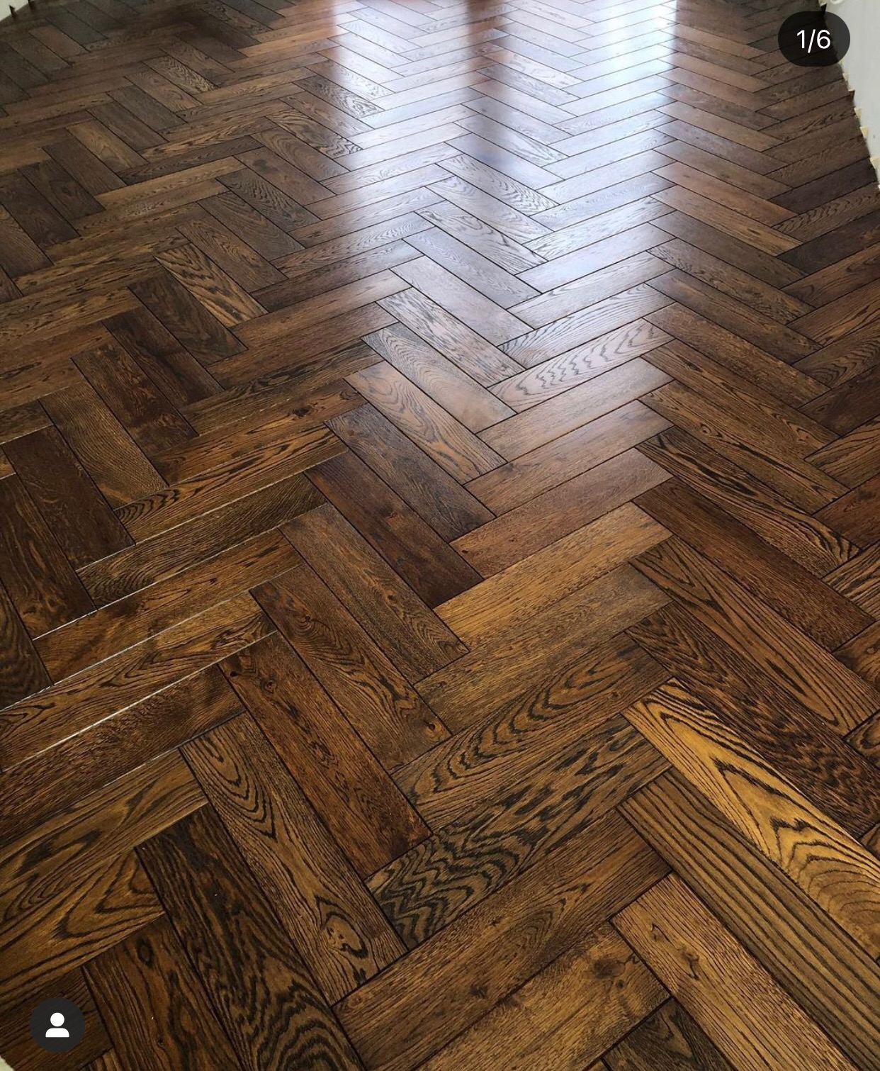 Ułożony parkiet w jodełkę, ciemne drewno z wyraźnym usłojeniem, wysoki połysk, widoczne odbicie światła od okna.