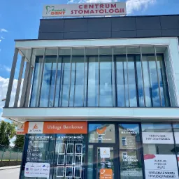 Fasada budynku z szyldami firm oferujących usługi bankowe, ubezpieczenia, nieruchomości, pomoc prawną oraz studio wizażu i stylizacji paznokci, z wyraźnym napisem 'Usługi Bankowe'...