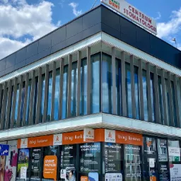 Budynek firmy finansowej Akywum z reklamami usług bankowych, leasingu, fotowoltaiki, ubezpieczeń i nieruchomości na oknach, pod błękitnym niebem.