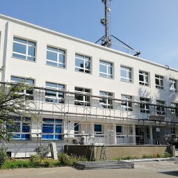 Total Partner Michał Semak - Budynek w Gorzowie Wielkopolskim z nowymi oknami, zabezpieczonymi folią i otoczony rusztowaniem, widoczne prace montażowe.