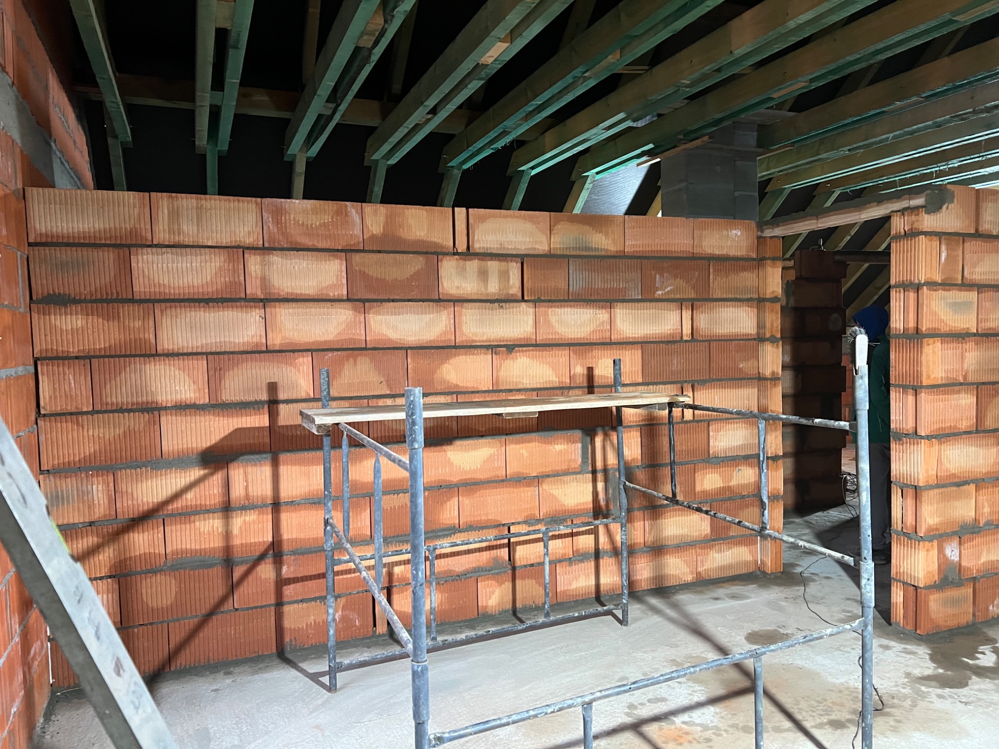 Wnętrze w trakcie budowy: ściany z czerwonej cegły, widoczne rusztowanie i drewniana konstrukcja dachu w surowym stanie.