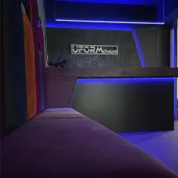 Recepcja biurowa z podświetleniem LED, logo firmy 'UFORMowANI' na ścianie i wielobarwna tapicerka sofy w nowoczesnym stylu.