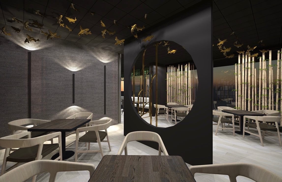 Nowoczesne wnętrze restauracji z ciemnymi ścianami, drewnianymi stołami i krzesłami w jasnych odcieniach. Dekoracyjne złote rybki zawieszone pod sufitem, okrągłe przejście do kolejnej sali...