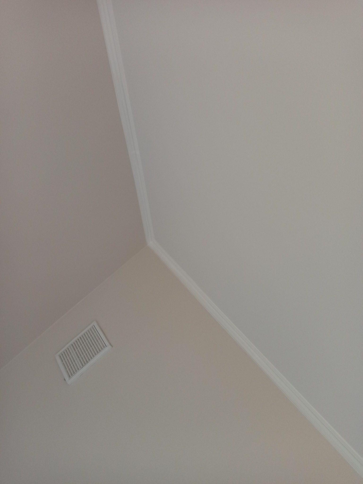 Pomieszczenie po remoncie, widok na róg sufitu z listwą dekoracyjną i kratką wentylacyjną, ściany pomalowane na dwa odcienie beżu.