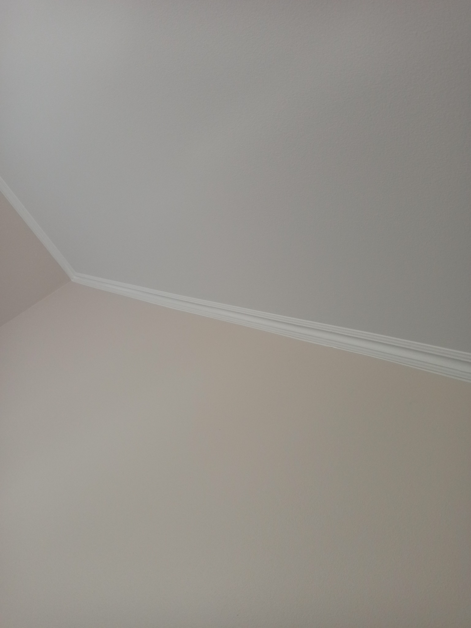 Fragment ściany i sufitu połączonych dekoracyjną, białą listwą przypodłogową, pomalowane na jasne, neutralne kolory.